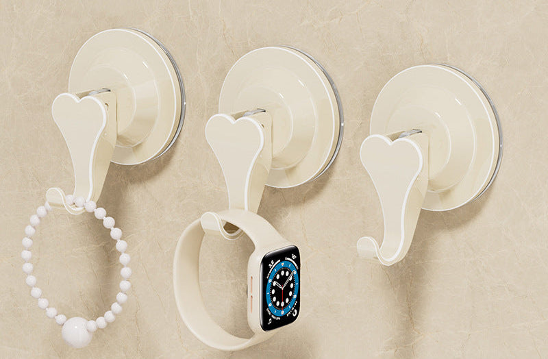 Three white suction cup hooks on a beige wall with a bracelet and smartwatch on display.